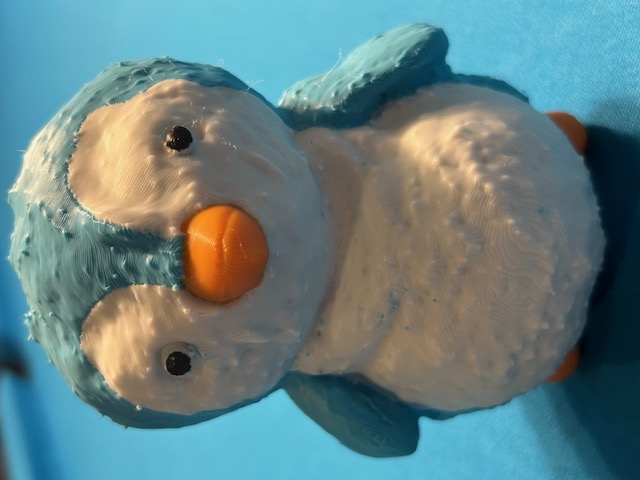 After: 3D-printed replica of the teal and white penguin with orange beak and feet, natural plastic finish